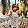 toddler, child, smiling, dress, barefoot, wooden_floor, outdoor, sunlight, railing, happy, girl, daylight, nature, person, playground, summer, cute, young_child, portrait, walking