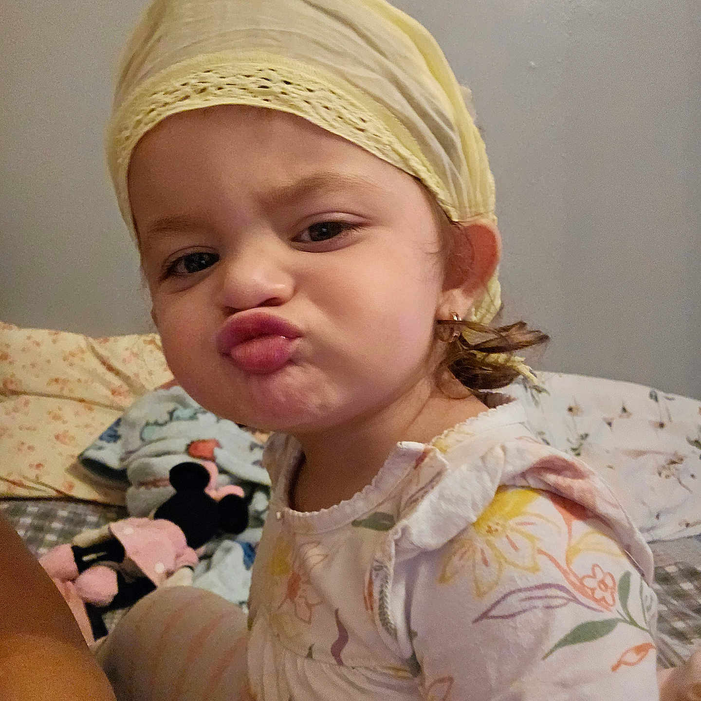 Daniela is registered to the contest to win money with this photo: bed, blanket, child, cute, earrings, expression, face, floral_pattern, headscarf, indoor, minnie_mouse, pajamas, person, plush_toy, portrait, pout, smile, soft_lighting, toddler, young_child