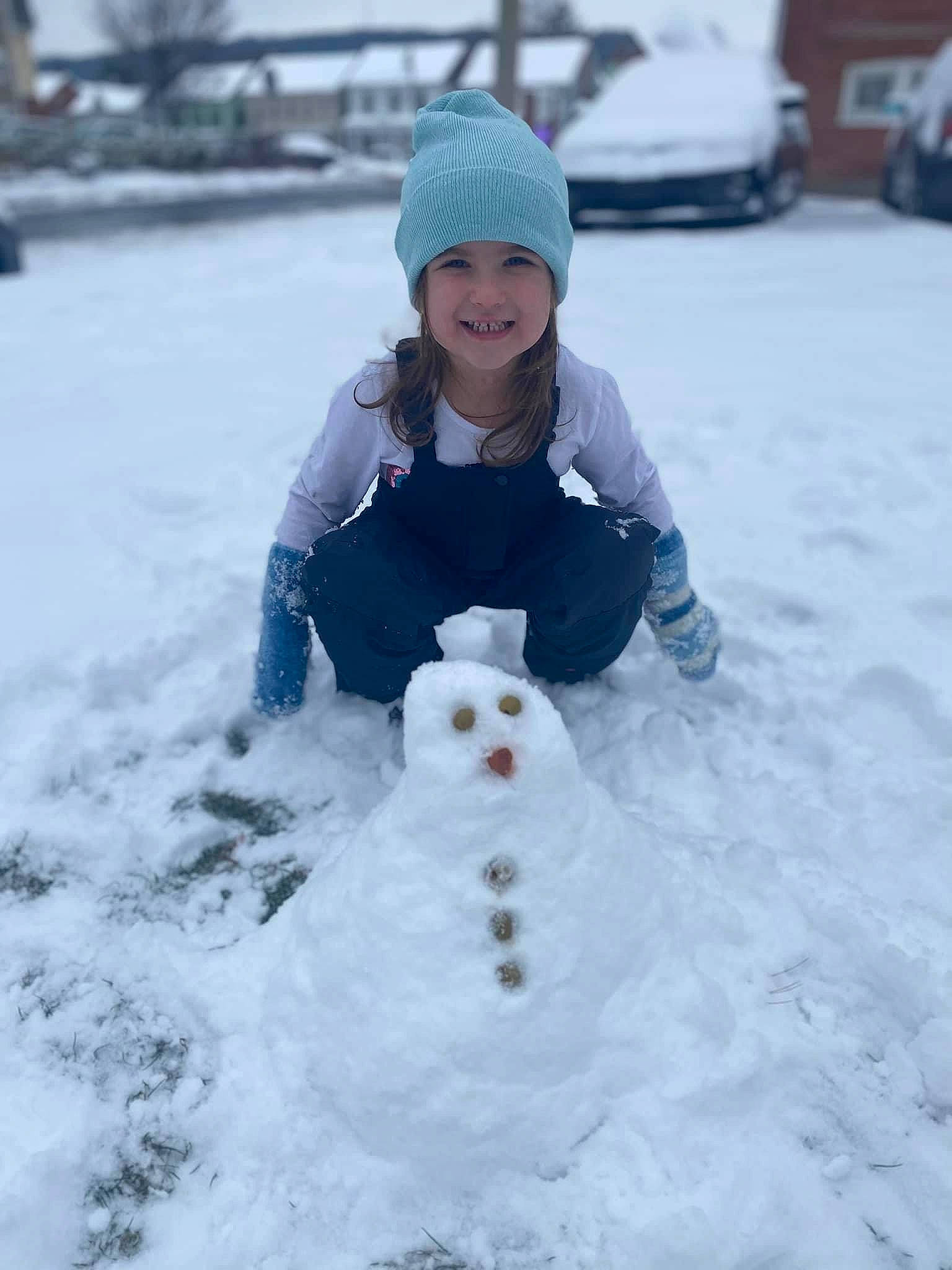 Zuri is registered to the contest to win money with this photo: beanie, child, face, freezing, frost, fun, fur, happy, headwear, joy, person, photograph, playing_in_the_snow, precipitation, recreation, sitting, smile, snow, snowman, toddler