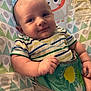 baby, bodypart, clothing, cushion, face, finger, furniture, hand, happy, head, homedecor, newborn, person, photography, portrait, quilt, shorts, sitting, smile, t_shirt