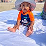 toddler, child, beach, hat, sunhat, orange_clothing, blue_clothing, blanket, sand, people, umbrella, summer, outdoor, sunny, portrait, baby, feet, sitting, vacation, casual