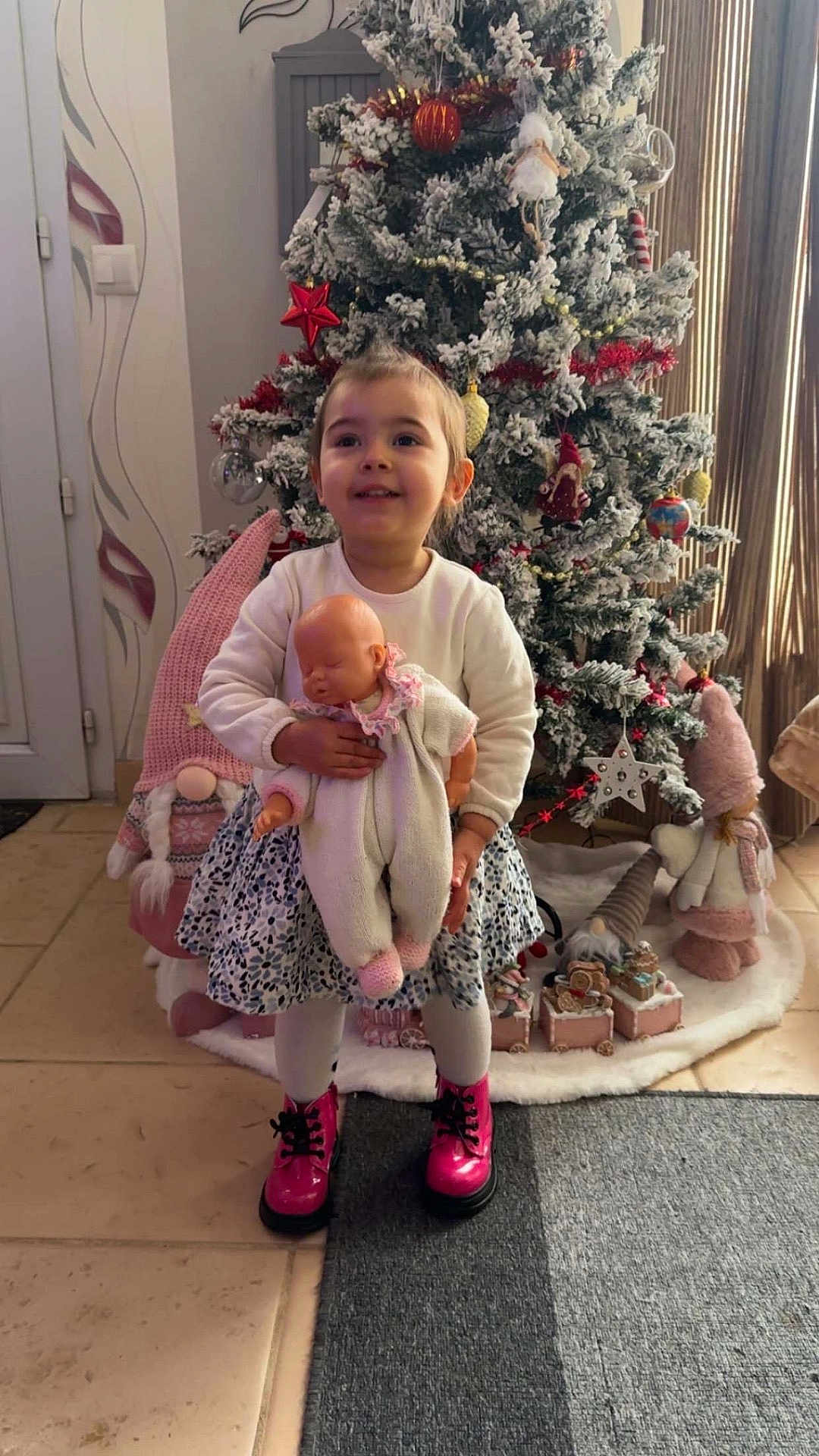 Kenzya participe au concours pour gagner de l'argent avec cette photo : child, girl, doll, christmas_tree, ornaments, holiday_decorations, pink_boots, floor, carpet, gnomes, white_tights, smiling, indoor, festive, toy, winter, happy, decor, celebration, seasonal