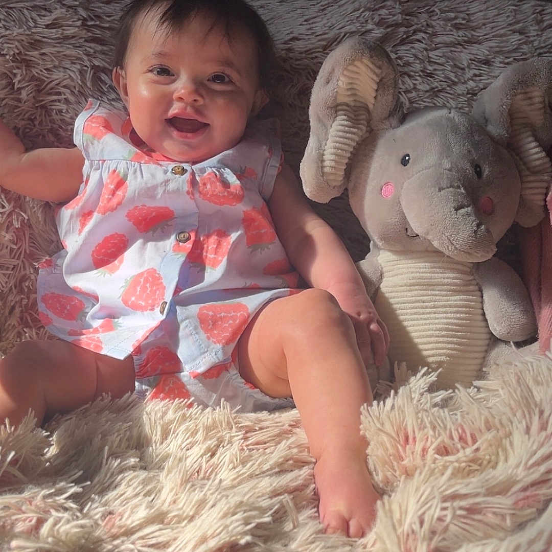 Storme joined the competition — help win amazing prizes! baby, blanket, child, clothing, cozy, cute, face, happy, indoor, infant, patterned_outfit, pink, plush_elephant, relaxing, sitting, smiling, soft_texture, stuffed_animal, sunlight, toy