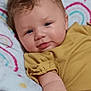 baby, infant, child, smile, face, blue_eyes, hair, blanket, rainbow_pattern, mustard_clothing, arm, cute, indoors, soft_texture, portrait, skin, hand, comfort, lying_down, happy