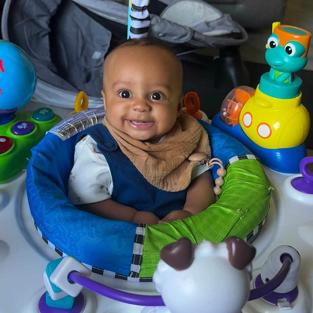 Zion joined the competition — help win amazing prizes! activity_center, baby, blue, child, clothing, colorful, face, floor, green, happy, head, indoor, infant, orange, person, play, seat, smiling, toy, yellow