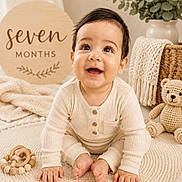 Luis Enrique is registered to the contest to win money with this photo: baby, infant, child, seven_months, sitting, smiling, happy, portrait, indoors, nursery, cream_colors, knitwear, rug, teddy_bear, teether, milestone_sign, plant, blanket, cozy, photography