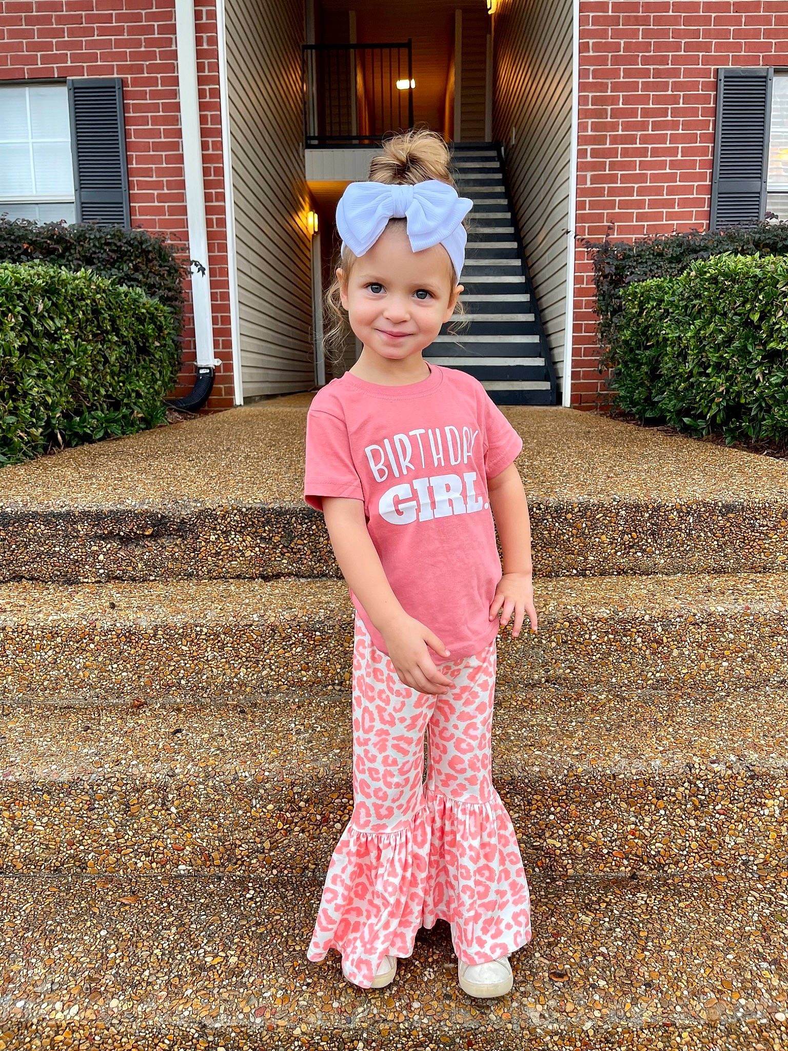 Jersey is registered to the contest to win money with this photo: baby_toddler_clothing, child, door, flooring, grass, happy, headgear, headwear, house, joy, lawn, leaf, magenta, people_in_nature, person, pink, plant, porch, sleeve, smile
