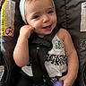 baby, black_and_white_clothing, bottle, car_seat, child, cute, face, happy, headband, holding, indoors, infant, person, playful, portrait, seatbelt, sitting, smiling, white_headband, young_child