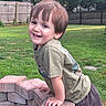 child, smiling, outdoor, grass, brick, greenery, fence, playful, happy, boy, casual_clothing, short_hair, daylight, nature, yard, person, cute, portrait, fun, leisure