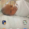 baby, newborn, infant, child, swaddled, blanket, lying_down, face, portrait, eyes_open, indoor, bed, white_clothing, soft_lighting, smartphone_screenshot, homescreen, weather_widget, mobile_apps, digital_photo, peaceful