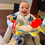 Sawyer joined the competition — help win amazing prizes! baby, child, infant, smiling, happy, portrait, indoor, activity_center, baby_toy, rattle, colorful, seated, playtime, bib, sock, stuffed_animal, wood_floor, home, face, date_stamp