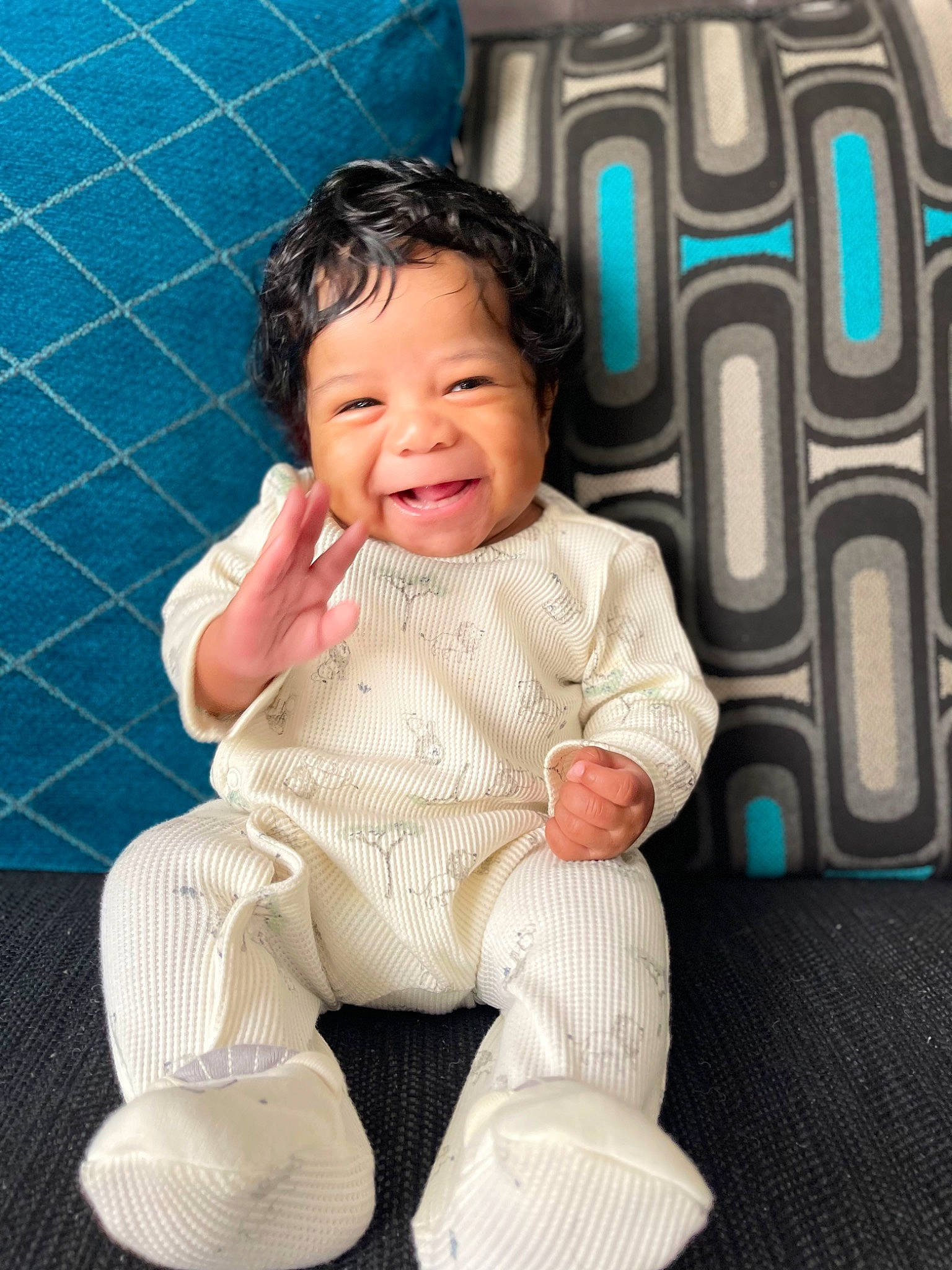 Callum is registered to the contest to win money with this photo: arm, baby, baby_toddler_clothing, cheek, child, comfort, facial_expression, finger, flooring, fun, happy, linens, pattern, person, product, sitting, skin, sleeve, smile, textile