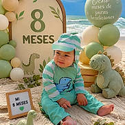 Edwin joined the competition — help win amazing prizes! baby, infant, dinosaur, plush_toy, balloons, beach, sand, blue_sky, ocean, milestone, sign, green_outfit, striped_clothing, cute, child, celebration, decorations, sitting, toes, nature