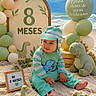 baby, infant, dinosaur, plush_toy, balloons, beach, sand, blue_sky, ocean, milestone, sign, green_outfit, striped_clothing, cute, child, celebration, decorations, sitting, toes, nature