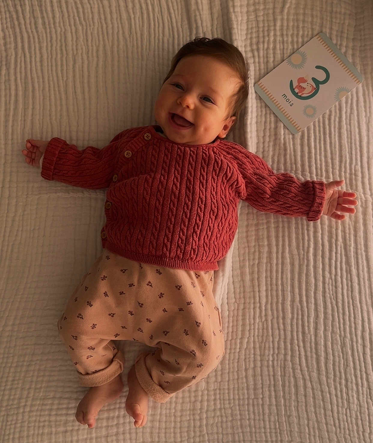Elena participe au concours pour gagner de l'argent avec cette photo : baby, infant, smiling, sweater, knit_sweater, pants, blanket, bedding, milestone_card, card, lying_down, bare_feet, hands, portrait, cozy, indoor, cute, happy, bed, soft_light