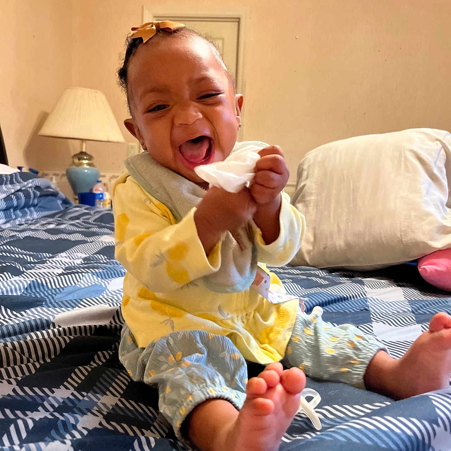 Nyiteeya is registered to the contest to win money with this photo: baby, bed, blanket, child, clothing, comfort, foot, hair_bow, happy, home, indoor, lamp, laughing, person, pillow, playful, room, sitting, smiling, tissue