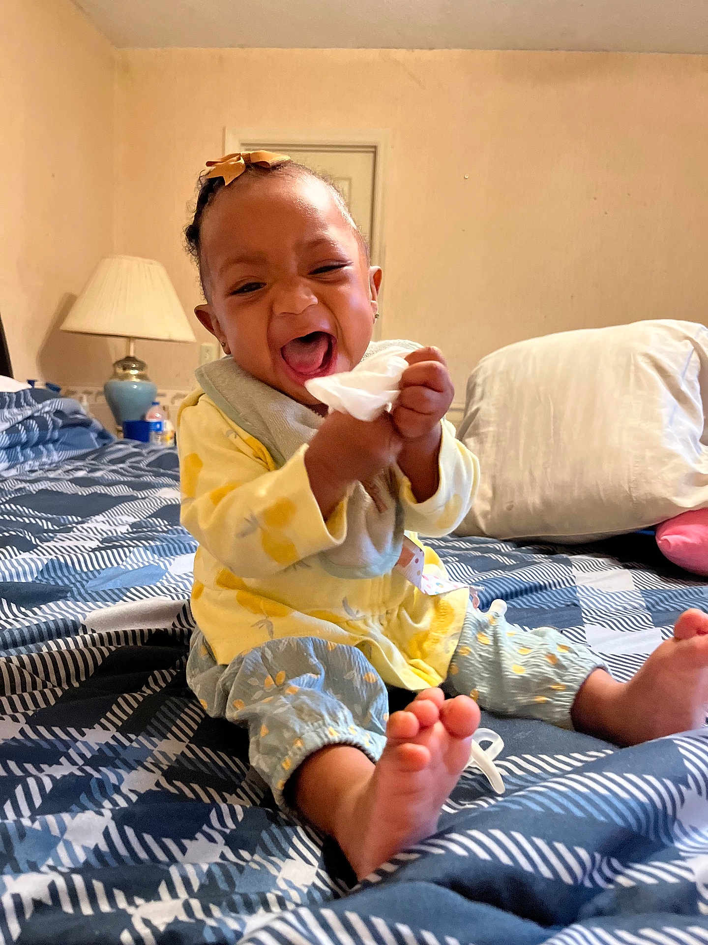 Nyiteeya is registered to the contest to win money with this photo: baby, child, smiling, laughing, bed, blanket, pillow, lamp, tissue, clothing, indoor, hair_bow, foot, sitting, room, comfort, happy, person, home, playful