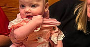 Sadie joined the competition — help win amazing prizes! baby, infant, child, birthday, party_hat, pink_clothing, smiling, sitting, portrait, family, adult, faces, wooden_background, indoors, celebration, cake_absent, baby_dress, lace, holding, happy