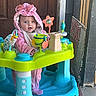 baby, child, infant, pink_hood, bow, smiling, sitting, activity_center, baby_toys, colorful, toy_fortress, portrait, indoors, doorway, wooden_door, playtime, happy, cute, bright_colors, floor_tiles