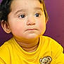 background, bear_patch, child, closeup, clothing, curious, cute, expression, eyebrows, eyes, face, hair, head, indoors, person, portrait, skin, toddler, yellow_shirt, young_child
