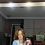 child, mirror, selfie, phone, reflection, indoor, cabinet, light, long_hair, casual_clothing, room, furniture, technology, portrait, holding, smile, young, home, repetition, curtain