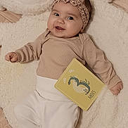 Victoire a rejoint le concours — aidez-le/la à gagner de superbes lots ! baby, child, clothing, cozy, cute, happy, headband, indoors, infant, leopard_print, lying_down, milestone_card, neutral_colors, person, plush_rug, portrait, sheep_shape, smile, soft_texture, wooden_floor