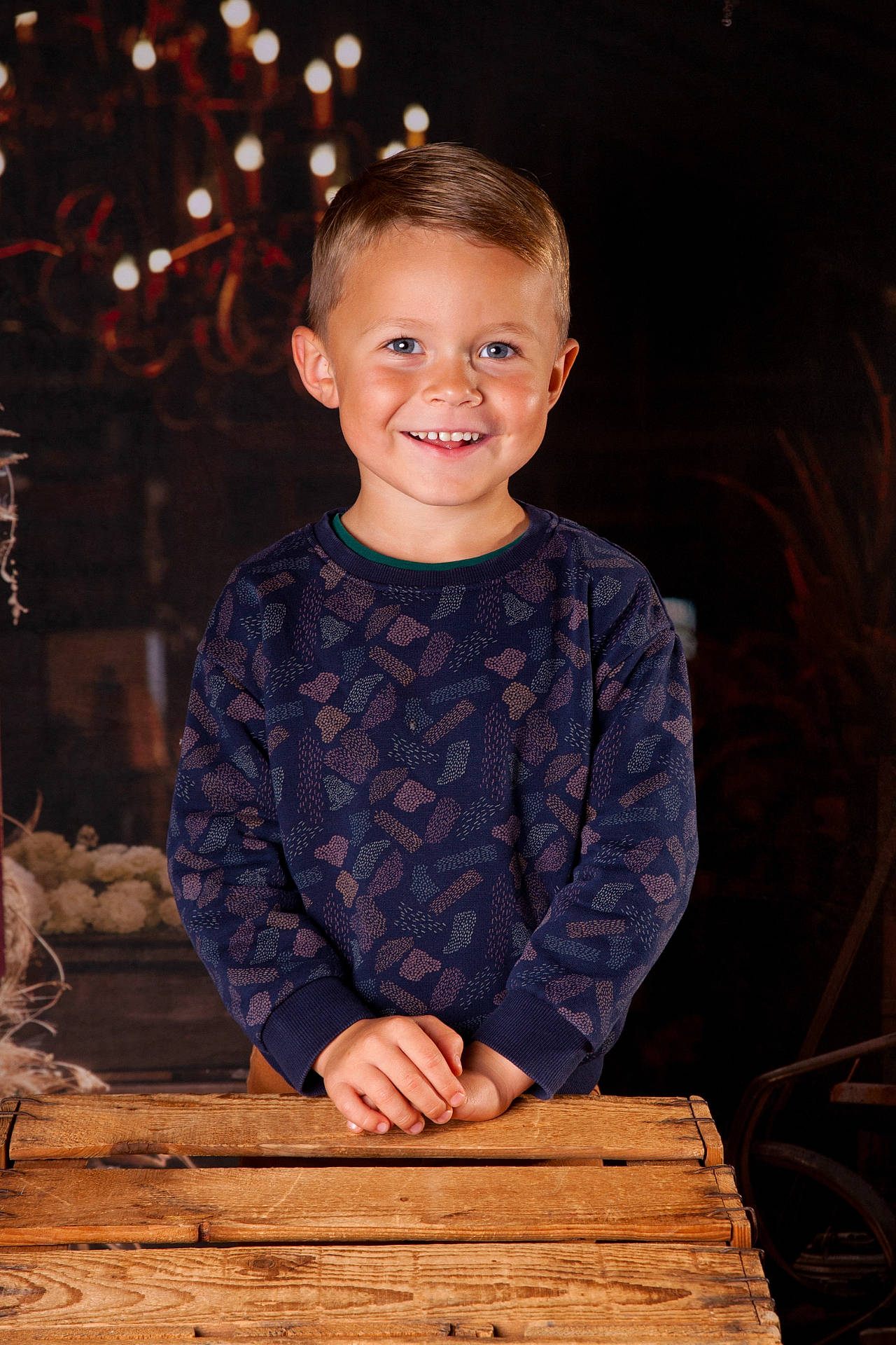 Côme a rejoint le concours — aidez-le/la à gagner de superbes lots ! background, blue_eyes, boy, casual_clothing, chandelier, child, cute, decor, flower_arrangement, hands, happy, indoor, lighting, patterned_sweater, portrait, short_hair, smiling, warm, wooden_table, young