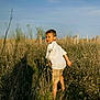child, boy, smile, barefoot, field, grass, sunlight, shadow, sky, nature, outdoor, summer, shorts, white_shirt, happy, walking, portrait, daylight, casual, young