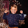 background, blond_hair, boy, candid, casual_clothing, cheerful, child, decor, dried_flowers, face, happy, indoor, playful, portrait, raised_fists, rustic, smile, sweater, warm_lighting, young