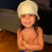 Raiteva a rejoint le concours — aidez-le/la à gagner de superbes lots ! bare_chested, blue_shorts, casual, child, close_up, couch, crossed_arms, face, happy, headscarf, home, indoor, long_hair, person, portrait, smiling, standing, warm_lighting, wooden_floor, young