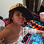 child, cap, tablet, playing, tongue_out, blanket, pajamas, indoor, popcorn, person, face, hand, colorful, pattern, bedroom, fun, casual, relaxed, technology, cute