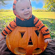 Leland is registered to the contest to win money with this photo: baby, pumpkin, jack_o_lantern, smiling, hoodie, orange, black, outdoor, grass, lake, trees, fall, seasonal, holiday, cute, child, face, happy, nature, costume