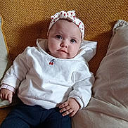 Myla participe au concours pour gagner de l'argent avec cette photo : baby, infant, child, headband, bow, white_sweater, cherry_embroidery, couch, cushion, pillow, textured_background, blue_eyes, smile, hand, legs, navy_pants, indoors, portrait, cozy, cute