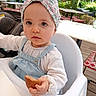 toddler, child, baby, high_chair, bread, food, headband, outdoor, cafe, table, chair, plants, wooden_floor, white_clothing, denim_overalls, face, hand, daylight, portrait, cute