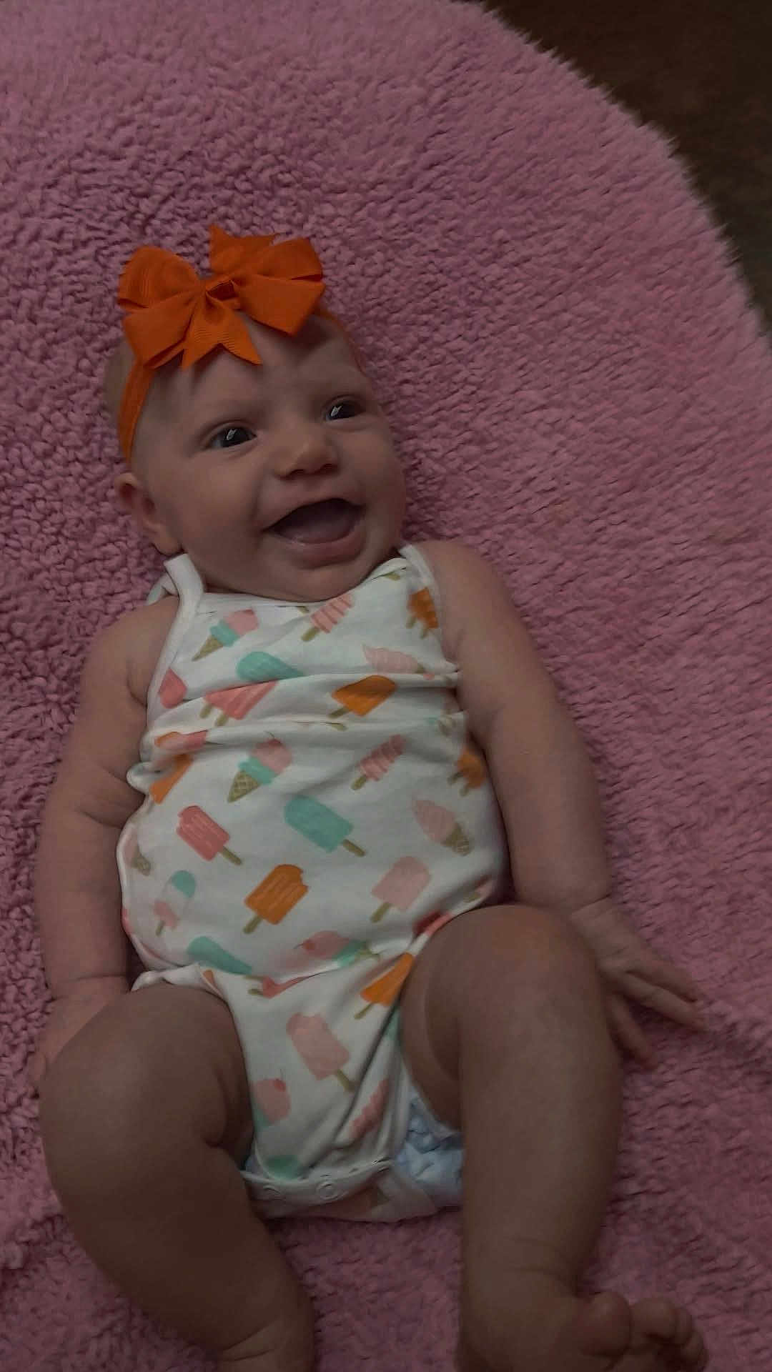 Aurora joined the competition — help win amazing prizes! baby, infant, smile, headband, bow, onesie, patterned_clothing, pink_blanket, soft_texture, happy, lying_down, cute, chubby_arms, chubby_legs, indoor, child, person, closeup, skin, baby_girl