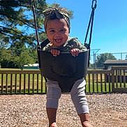 Anaya is registered to the contest to win money with this photo: child, toddler, swing, playground, outdoor, smiling, happy, headband, tree, sky, sunlight, grass, fence, barefoot, clothing, person, fun, play, woodchips, daytime