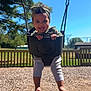 child, toddler, swing, playground, outdoor, smiling, happy, headband, tree, sky, sunlight, grass, fence, barefoot, clothing, person, fun, play, woodchips, daytime