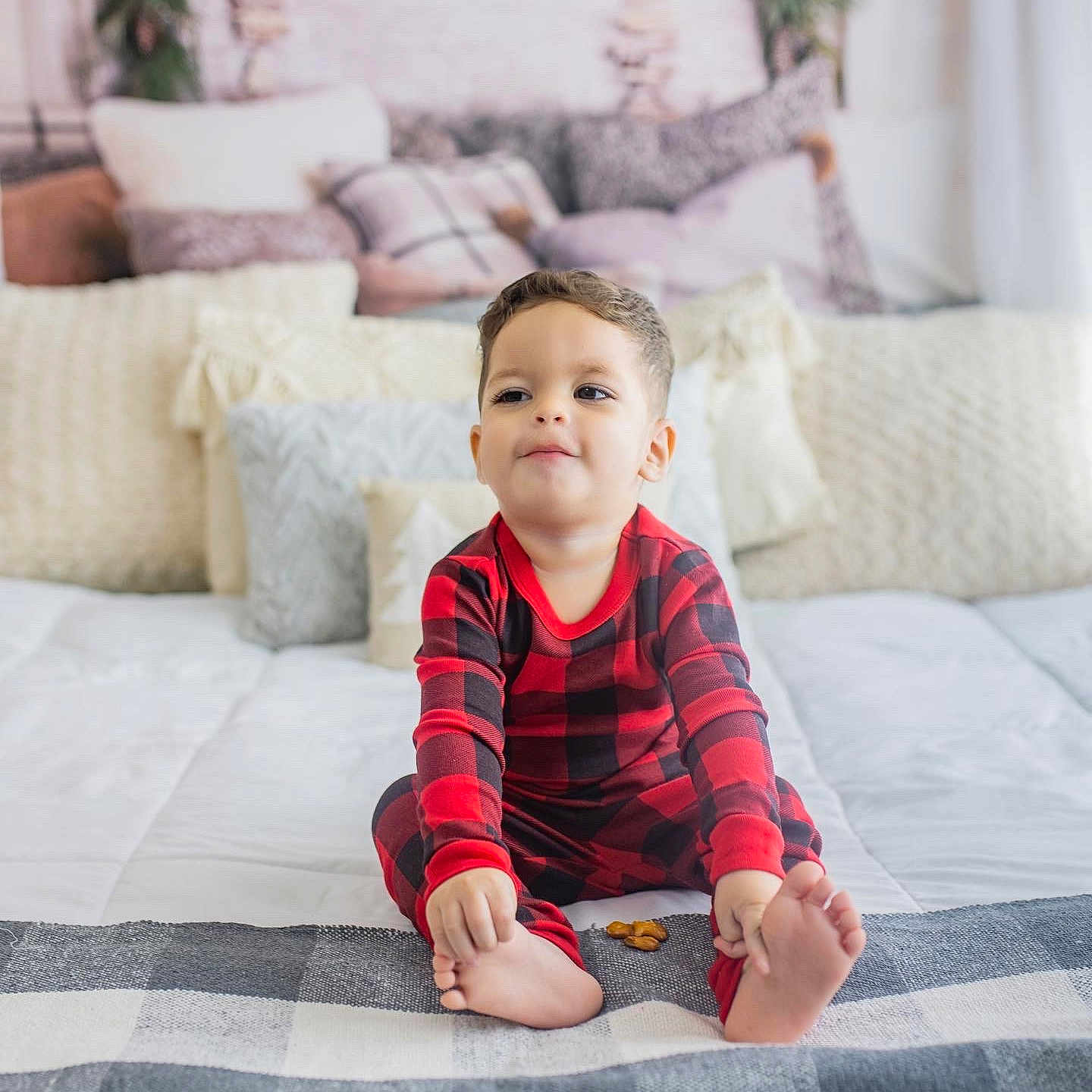 Gianluca is registered to the contest to win money with this photo: bed, black, blanket, child, comfort, cozy, cute, face, feet, home, indoor, pajamas, person, pillows, plaid, red, sitting, smiling, snack, toddler