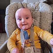 Bentley is registered to the contest to win money with this photo: baby, child, high_chair, dinosaur_print, yellow_shirt, mohawk, smile, happy, indoors, face, person, seatbelt, straps, clothing, infant, cute, portrait, kitchen, home, expression