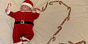 Timéo a rejoint le concours — aidez-le/la à gagner de superbes lots ! baby, blanket, candy_cane, celebration, child, christmas, cute, decoration, festive, footwear, holiday, indoors, infant, lying_down, portrait, red_clothing, santa_claus_costume, seasonal, smiling_face, soft_texture