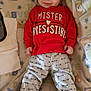 baby, infant, smiling, red_sweatshirt, gray_pants, arrows, blanket, teddy_bear_pattern, stars, socks, cozy, cute, child, young_child, indoors, portrait, lying_down, clothing, happy, face