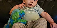 Corsen is registered to the contest to win money with this photo: baby, child, plush_toy, dinosaur_toy, sofa, leather, clothing, pants, tshirt, sitting, indoor, person, cute, infant, young_child, face, expression, hand, foot, cozy
