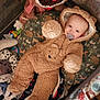 Corsen is registered to the contest to win money with this photo: baby, child, onesie, bear_costume, plush_toy, playpen, pacifier, blanket, stuffed_animal, toy, face, infant, cute, indoor, soft_toy, head, clothing, lying_down, comfort, childcare