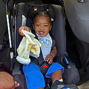 Jurnee is registered to the contest to win money with this photo: baby, blanket, blue_shorts, car_interior, car_seat, child, cute, hair_puffs, hand, infant, joyful, person, playful, safety, seatbelt, sitting, smiling, sneakers, toddler, white_shirt