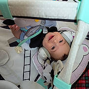 Alexander is registered to the contest to win money with this photo: baby, child, smiling, headphones, toy, play_mat, soft_toy, indoor, infant, cute, baby_clothing, play_gym, cushion, happy, lying_down, face, person, floor, colorful, comfort