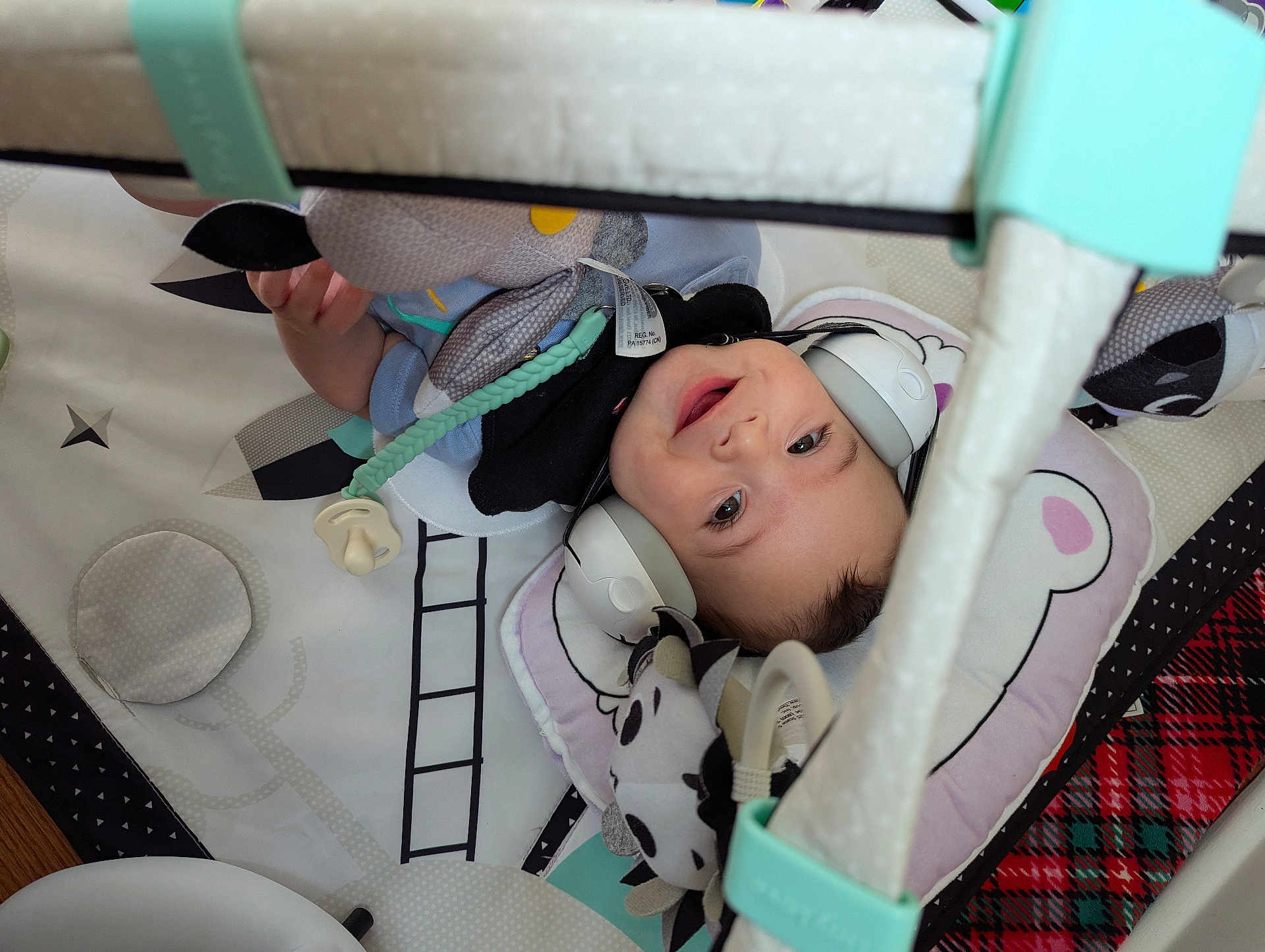 Alexander is registered to the contest to win money with this photo: baby, child, smiling, headphones, toy, play_mat, soft_toy, indoor, infant, cute, baby_clothing, play_gym, cushion, happy, lying_down, face, person, floor, colorful, comfort