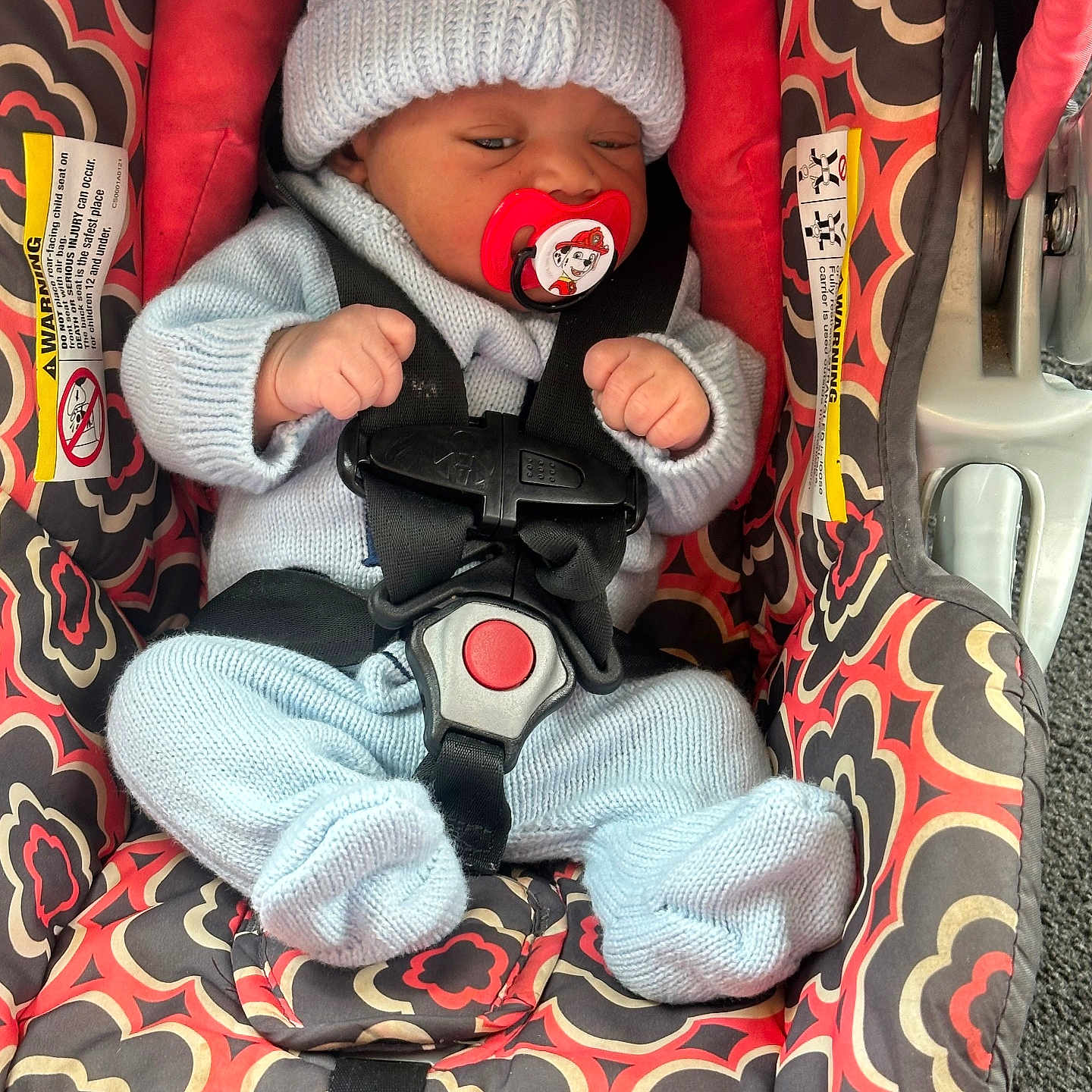 Joeray joined the competition — help win amazing prizes! baby, infant, car_seat, pacifier, knitted_hat, knitted_clothing, safety_harness, patterned_fabric, red, blue, child, seat_belt, indoor, cute, newborn, small_hands, small_feet, resting, child_safety, car_accessory
