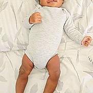 Victor is registered to the contest to win money with this photo: baby, infant, onesie, bed, blanket, pattern, hand, foot, skin, lying_down, cute, child, newborn, person, sleepwear, indoors, resting, fist, smiling, playful