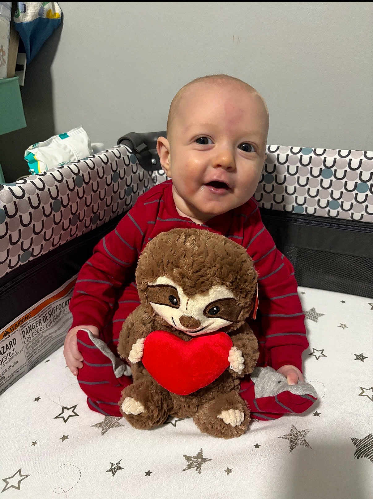 Weston joined the competition — help win amazing prizes! baby, infant, child, smiling, plush_sloth, stuffed_animal, red_pajamas, playpen, crib, heart, toy, portrait, cute, happy, face, sitting, bedding, stars_pattern, indoor, blanket
