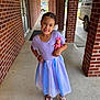 child, girl, smiling, dress, doll, sandals, bracelet, brick_wall, sidewalk, outdoor, portrait, happy, person, toy, footwear, building, window, door, concrete, sunlight